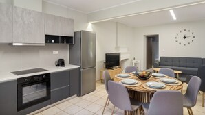 A modern kitchen with a built-in oven, a refrigerator, and a dining area with a round table set for four. - Holiday Home 'Sparto' with Private Terrace, Wi-Fi and Air Conditioning (Spartochori)