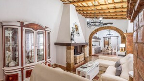 Un salon avec une cheminée, un coin repas et une cuisine ouverte sur le salon par une arche.