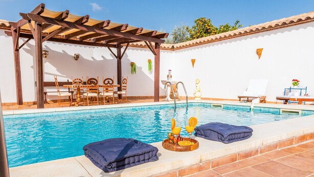 Une piscine agrémentée d’une pergola, de chaises longues et d’une table où sont servis des boissons.