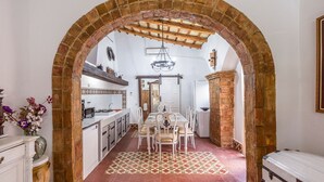 Un intérieur agrémenté d’une arche en briques menant à une salle à manger, d’une cuisine avec des meubles blancs et d’un sol à motifs.