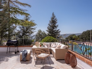 An outdoor patio with a sofa, chairs, a grill, and a pool.