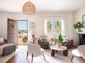 A living room with a sofa, chairs, a coffee table, a hanging light fixture, and a window with curtains.