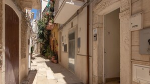 Une ruelle étroite bordée d’immeubles en pierre, avec une porte en bois et un coffret électrique sur le côté droit.