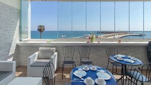 Une terrasse avec vue sur la mer, des meubles en osier et une table dressée pour le dîner.
