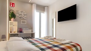 Ett hotellrum med en säng, en tv, en växt, en väggdekoration med fiskmotiv och ett fönster med gardiner.
