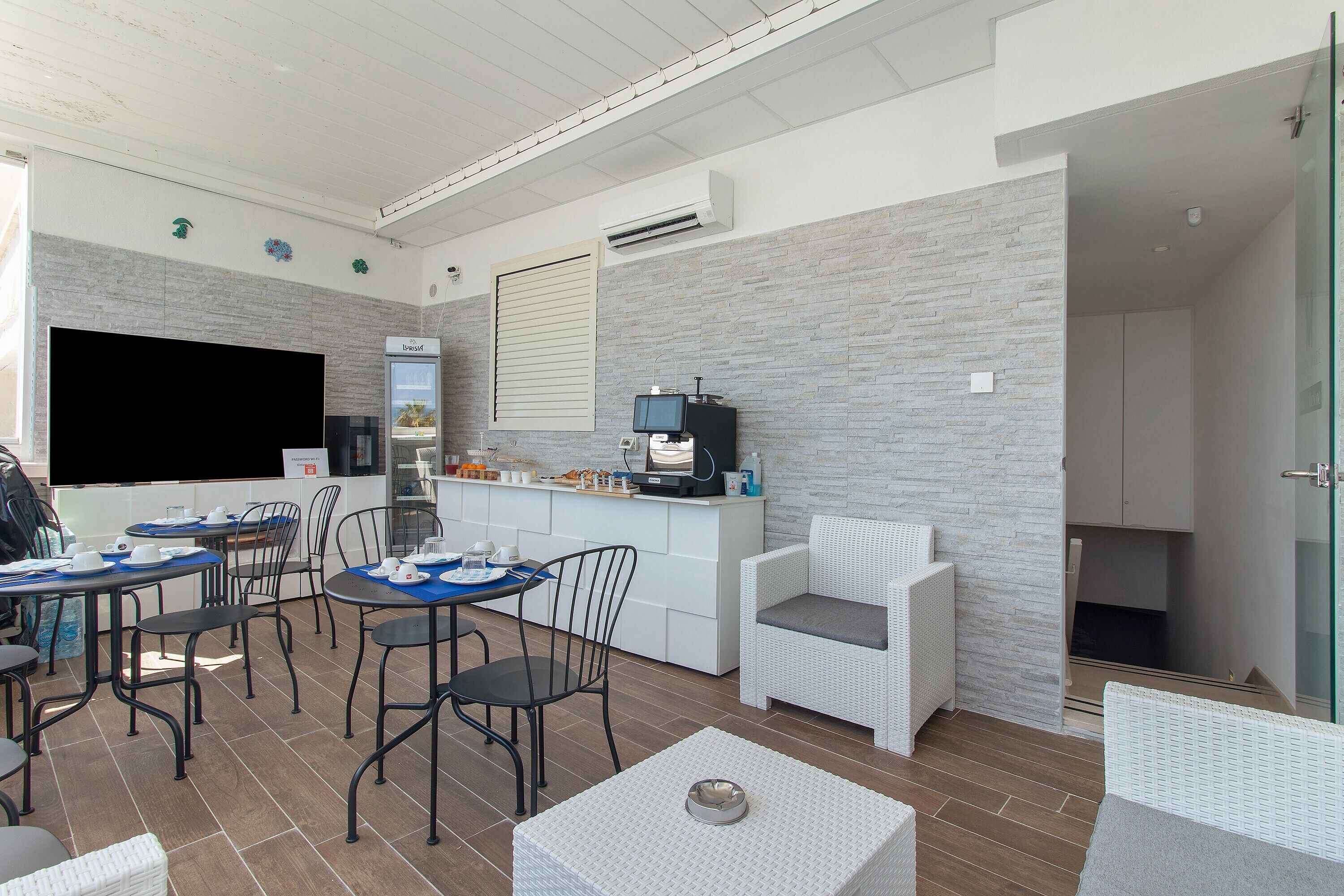 A modern kitchen with a flat-screen TV, dining area with chairs and tables, and a small seating area with a sofa.