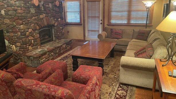 A cozy living room with a stone fireplace, a wooden coffee table, patterned sofas, and a television. - 3 BRD Apartment (Bigfork)