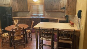 A rustic kitchen with wooden cabinets, a central island, and a dining area with wooden chairs. - 3 BRD Apartment (Bigfork)