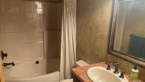 A bathroom with a bathtub, toilet, sink, and a large mirror. - 3 BRD Apartment (Bigfork)