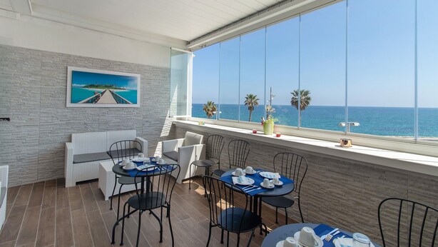 A balcony with a view of the sea, furnished with tables and chairs, and a painting on the wall. - Room 'Stella Marina' with Shared Terrace, Wi-Fi and Air Conditioning (Mola di Bari)