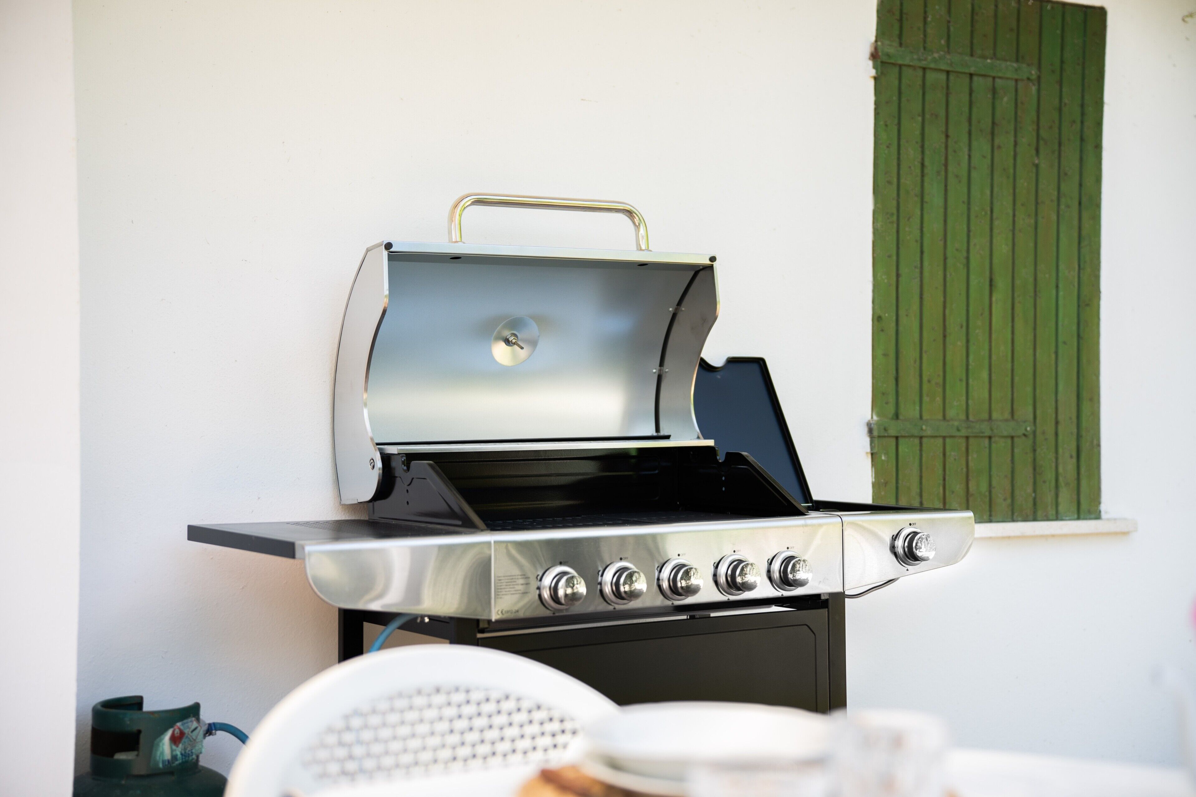 Una parrilla de acero inoxidable con un asa, cuatro perillas y una puerta de horno negra.