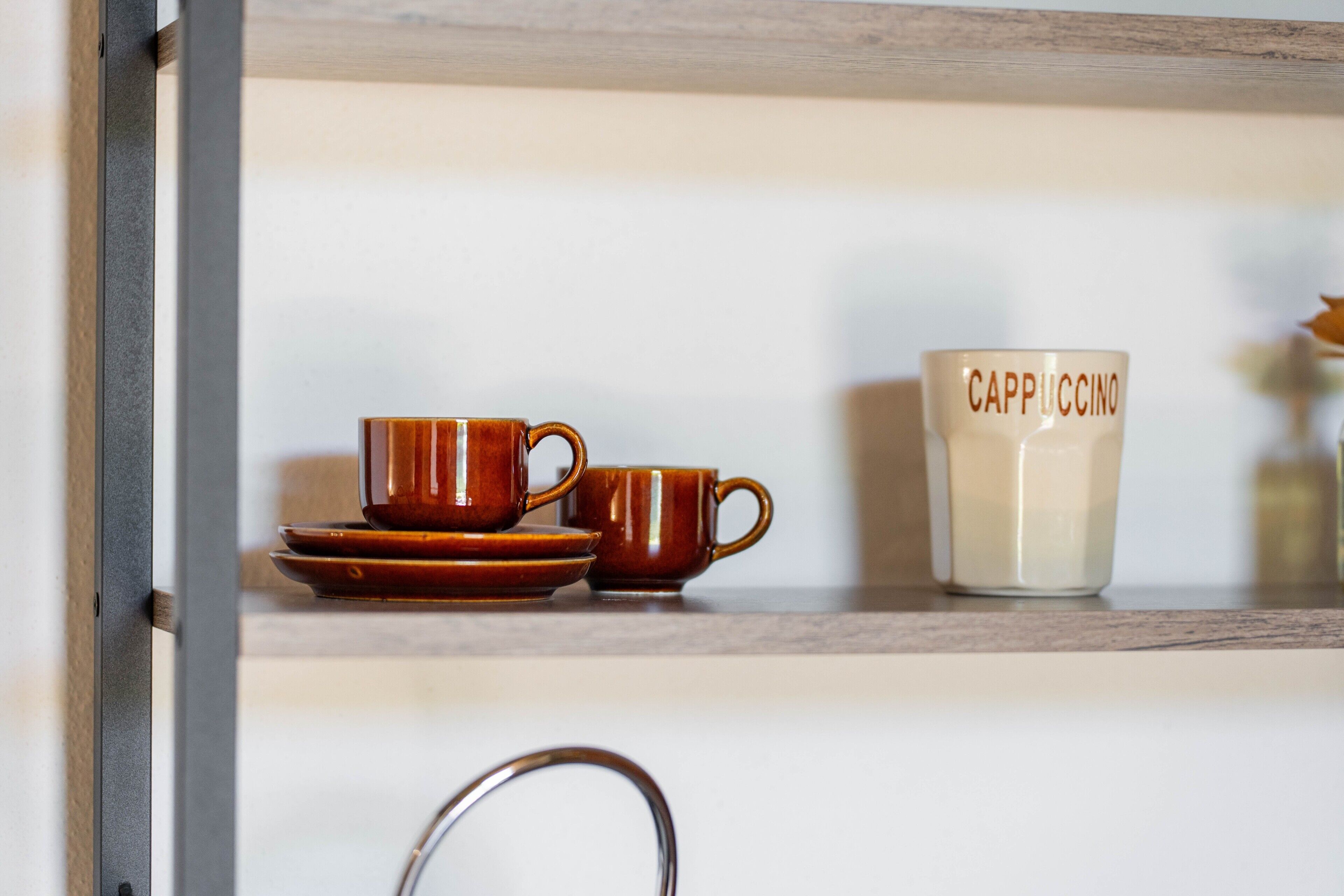 A shelf with a set of brown cups and saucers, and a white cup with 'Cappuccino' written on it.