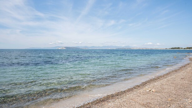 Una spiaggia con acqua calma, riva di ciottoli e montagne sullo sfondo.