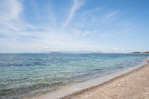 A clear view of a beach with calm water, pebbly shore, and distant mountains.