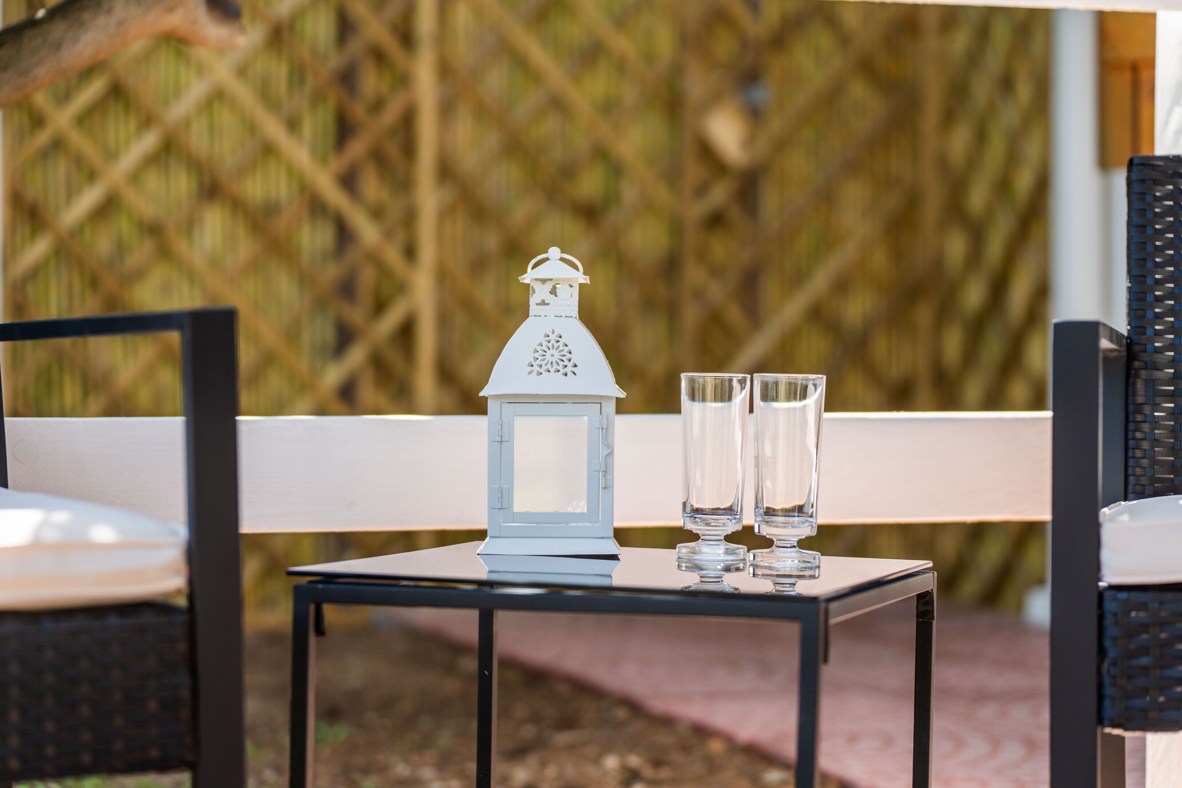 Una mesa con un farol blanco y tres vasos, sobre un fondo de celosía.