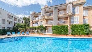 A swimming pool with lounge chairs, a multi-story building with balconies, and a clear sky. - Apartment 'Llenaire' with Mountain View, Wi-Fi and Air Conditioning (Port de Pollença)