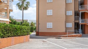 A multi-story building with balconies, a parking area with marked spaces, and a palm tree in the background. - Apartment 'Llenaire' with Mountain View, Wi-Fi and Air Conditioning (Port de Pollença)