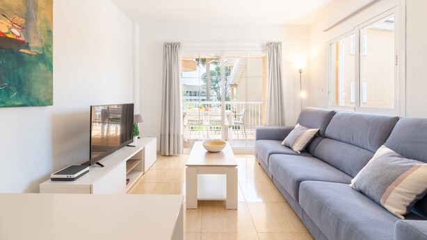 A modern living room with a grey sofa, a flat-screen TV, a coffee table, and a balcony with outdoor furniture. - Apartment 'Llenaire' with Mountain View, Wi-Fi and Air Conditioning (Port de Pollença)
