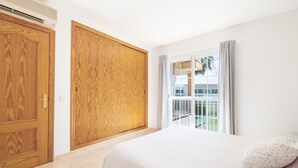 A bedroom with a bed, wooden wardrobe, and a balcony with a view. - Apartment 'Llenaire' with Mountain View, Wi-Fi and Air Conditioning (Port de Pollença)