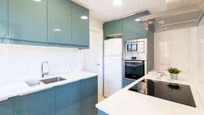 A modern kitchen with teal cabinets, a white countertop, a built-in oven, and a black induction cooktop. - Apartment 'Llenaire' with Mountain View, Wi-Fi and Air Conditioning (Port de Pollença)