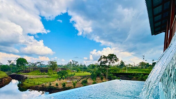 A swimming pool with a waterfall feature, surrounded by a natural landscape and a clear sky. - HOTEL FINCA PROCEL (Palora)