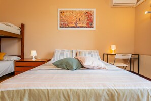 Une chambre d’hôtel avec un lit superposé, un lit simple, une lampe, une chaise et un tableau au mur.