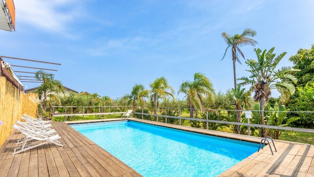 Eine Holzterrasse mit Schwimmbecken, umgeben von Palmen und viel Grün.
