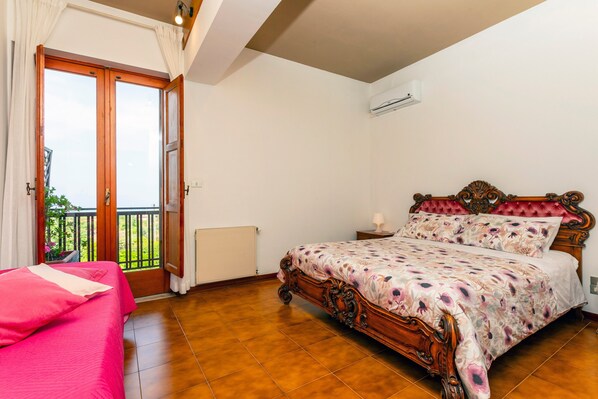 Un dormitorio con cama de madera, puerta al balcón y equipo de aire acondicionado.
