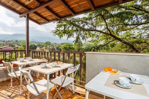 Un patio al aire libre con mesas y sillas, una pérgola de madera y vistas a un paisaje montañoso.