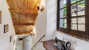 Ein Zimmer mit Holzboden, einer Nähmaschine, einem Fenster mit Außenblick und Wandleuchten.