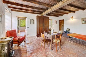 A rustic room with a wooden table, chairs, a sofa, and a bed with a red bedspread.