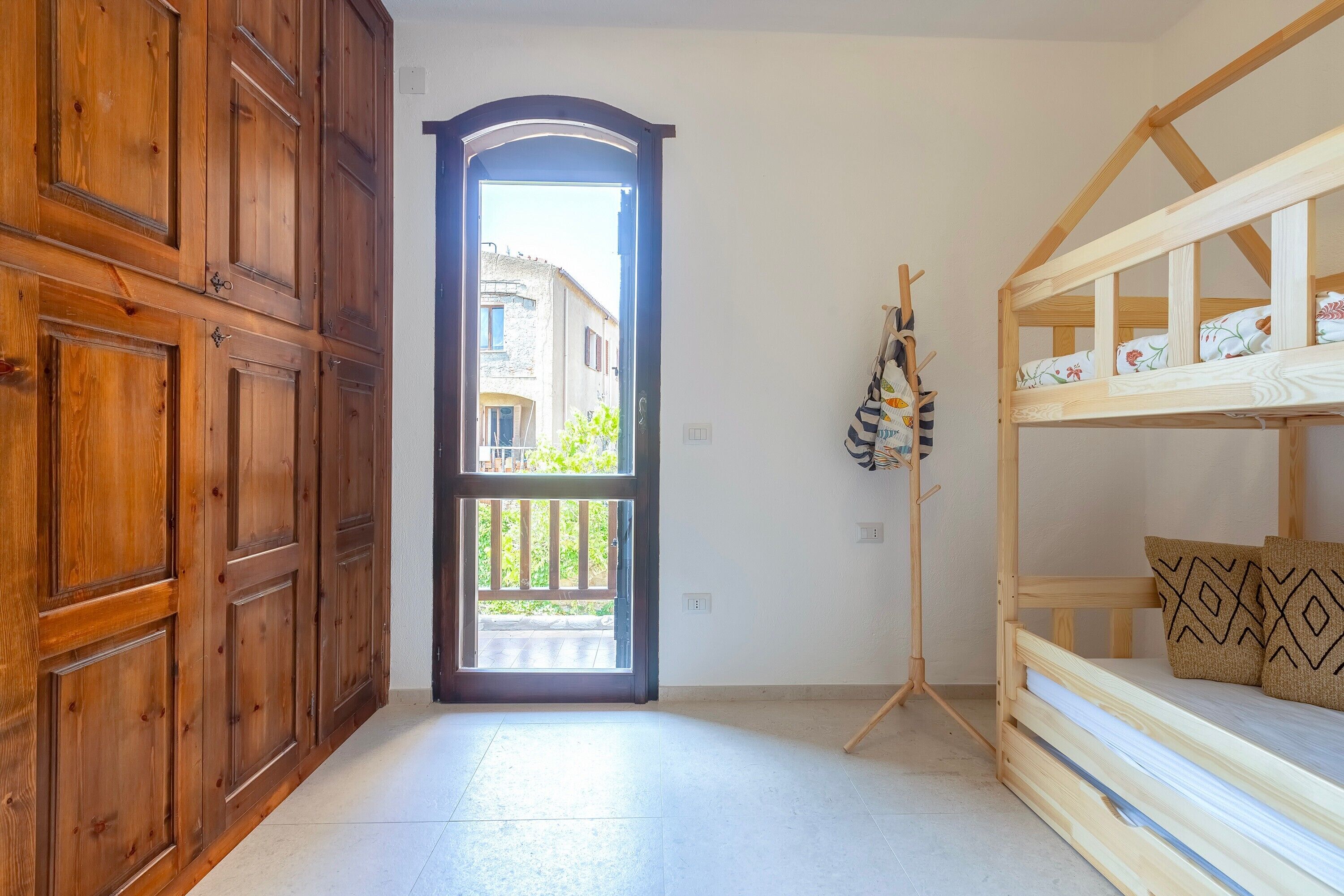 Habitació amb armari de fusta, llit amb coixins estampats i vista per una porta.