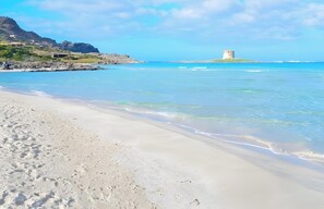 Una playa con agua cristalina, una orilla de arena y una torre en una pequeña isla.