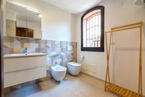 Un baño moderno con bidé, inodoro y un tendedero de madera.