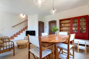 Un coin repas avec une table et des chaises en bois, un buffet rouge aux portes vitrées et un escalier menant à un autre niveau.