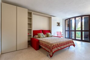 Un dormitorio con cama, armario, un banco rojo y un ventanal grande.