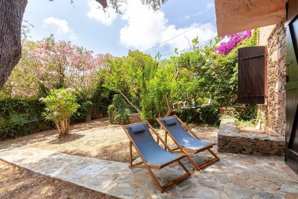 Un patio de piedra con dos sillones de descanso, rodeado de vegetación y un muro de piedra.