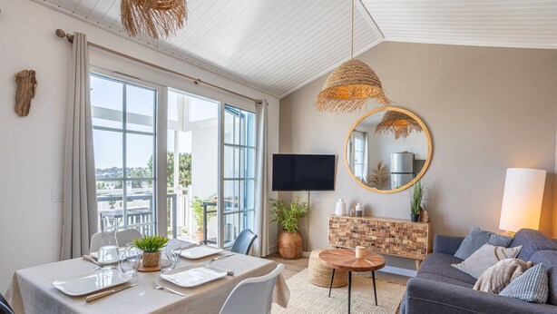 A modern living room with a dining area, a television, and a view of the city. - Apartment 'La Terrasse Du Golf' with Shared Pool, Private Terrace and Balcony (Talmont-Saint-Hilaire)
