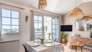 A dining area with a table set for two, a television, and a view of the outdoors. - Apartment 'La Terrasse Du Golf' with Shared Pool, Private Terrace and Balcony (Talmont-Saint-Hilaire)