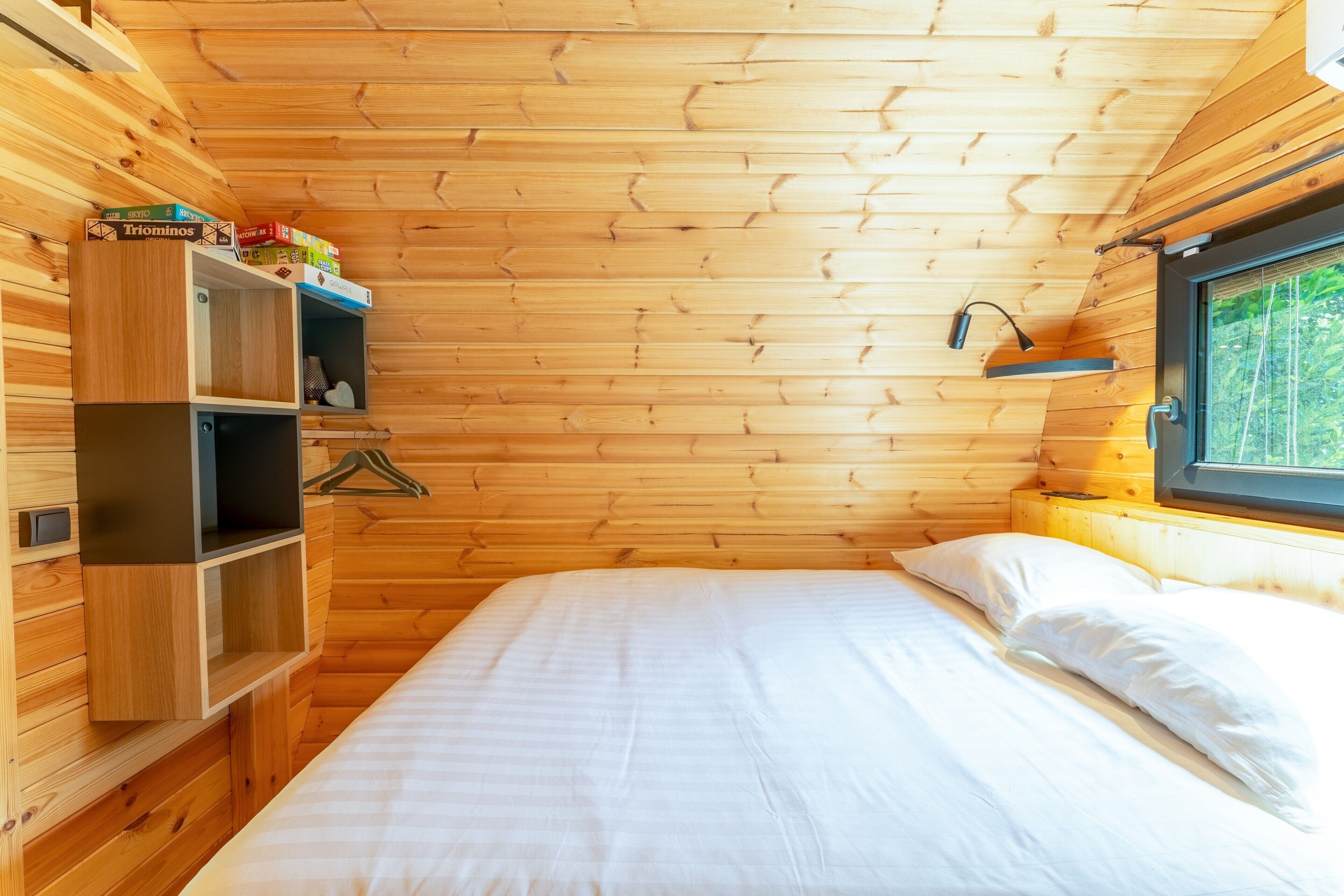 A wooden-paneled room with a bed, shelves, and a window.
