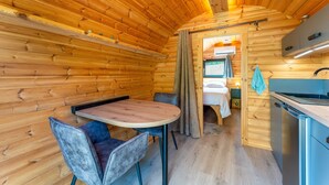 A wooden cabin interior with a dining area, a kitchenette, and a sleeping area. - Unique 'Prestige Barrel' Cottage with Private Pool, Wi-Fi, and Air Conditioning (Jonquières)