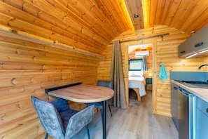 A wooden cabin interior with a dining area, a kitchenette, and a sleeping area. - Unique 'Prestige Barrel' Cottage with Private Pool, Wi-Fi, and Air Conditioning (Jonquières)