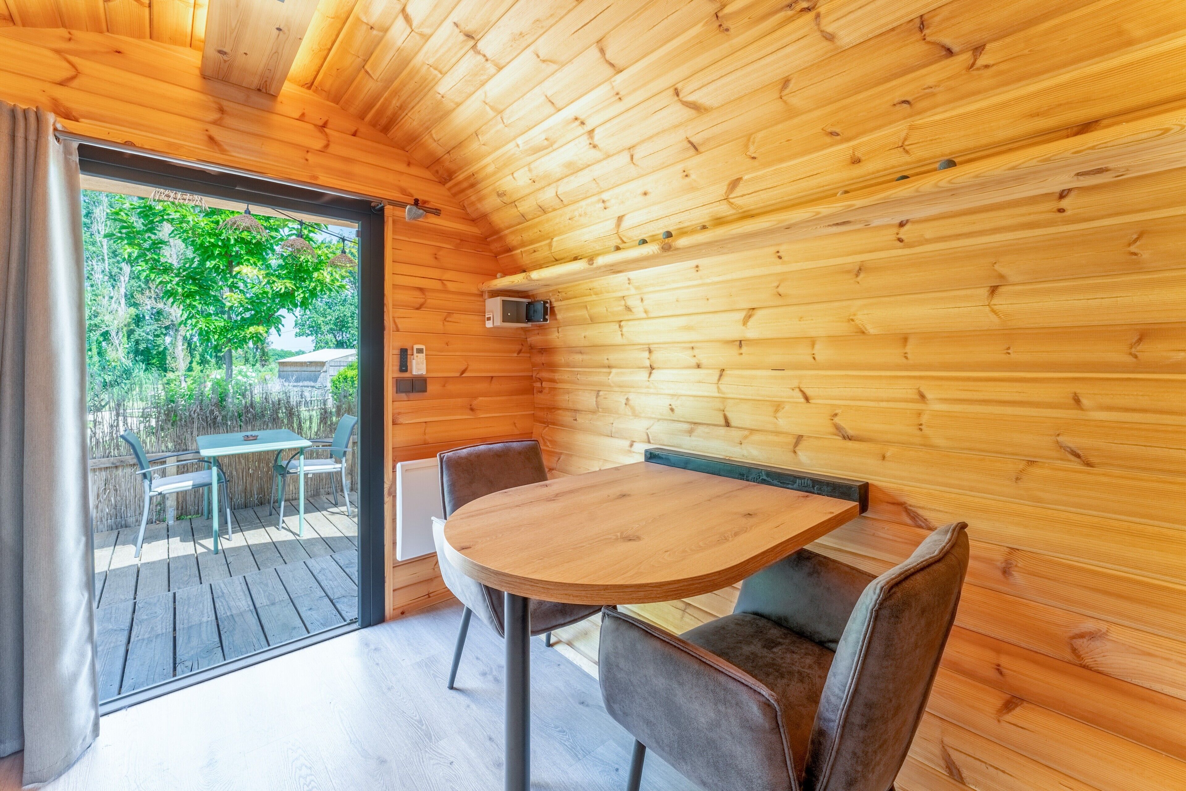 Ein Holzinnenraum mit einem runden Tisch und Stühlen, einer Schiebetür zu einer Terrassenfläche und einer Decke mit sichtbaren Holzbalken.