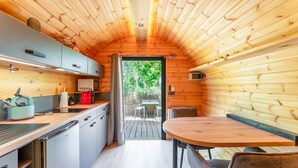 A compact, wooden cabin interior with a kitchenette, dining area, and a door leading to an outdoor deck. - Unique 'Prestige Barrel' Cottage with Private Pool, Wi-Fi, and Air Conditioning (Jonquières)