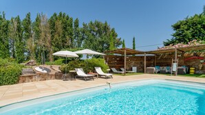 A swimming pool with lounge chairs and umbrellas, surrounded by trees and a wooden pergola. - Unique 'Prestige Barrel' Cottage with Private Pool, Wi-Fi, and Air Conditioning (Jonquières)