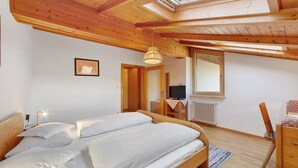 Een slaapkamer met een houten plafond, een bed met wit beddengoed, een bureau met een stoel, en een televisie.