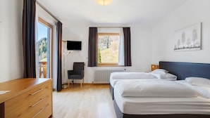 A bedroom with two beds, a desk, a chair, a radiator, a TV, and a window with curtains. - Gasthof Kirchsteiger 'Zimmer 5' with Lake View, Shared Terrace and Wi-Fi (Santa Valburga)