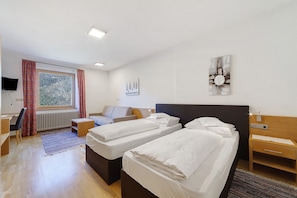 Une chambre d’hôtel avec deux lits, un bureau, une chaise, un radiateur et une fenêtre avec des rideaux.