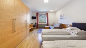 Ein Schlafzimmer mit Holzschrank, Bett, Schreibtisch und einem Fenster mit Vorhängen.