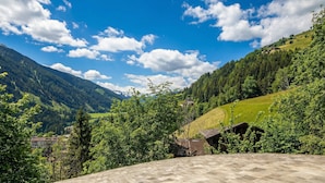 Eine gebirgige Landschaft mit blauem Himmel, grünen Hügeln und einigen Gebäuden.